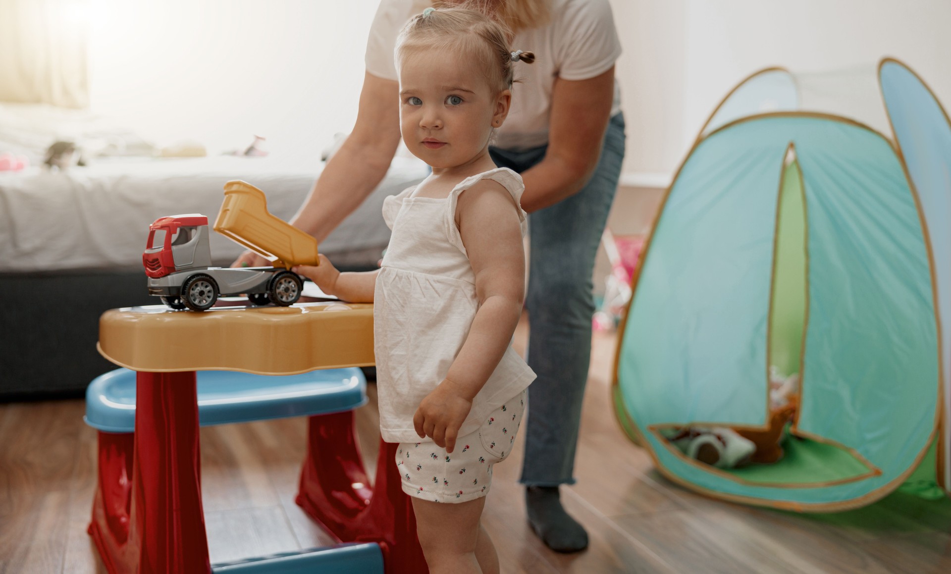 Little girl having fun with mom in playing room at home and looking camera